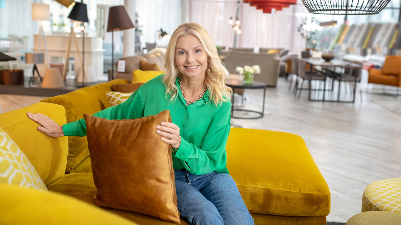 Frau mit grüner Bluse sitzt auf einem gelben Sofa und lächelt in die Kamera